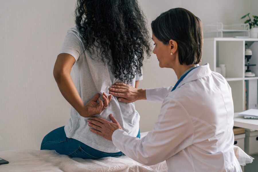 Faceless african-american female patient complaining about painful rheumatism to orthopedist. Muscular office syndrome sparm. Therapist touching and examining spine. Physician consultation