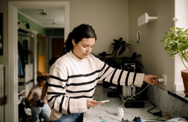 Woman charging smart phone while standing near kitchen counter at home